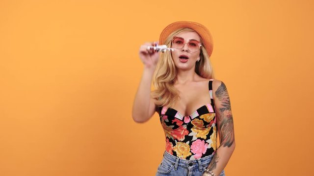 Sexy tattooed woman playing with a toy airplane in travel and holiday concept footage over yellow background. Sensual taned blonde