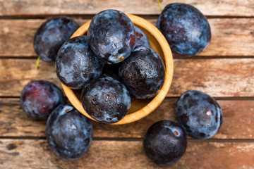 Fresh ripe plums in wooden bowl top view