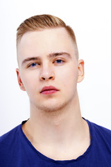 Fototapeta premium Young blond man in blue shirt poses in studio, close up portrait