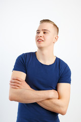 Young happy handsome man in blue shirt and jeans poses with crossed arms in white studio