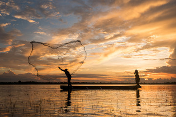 Two fisherman cast a net at lake in the moring time , silhouette light