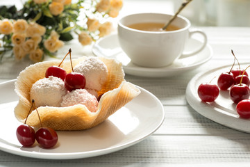 On a wooden white table are plate with the waffle basket with dessert, decorated  cherry berries , cup of tea and roses