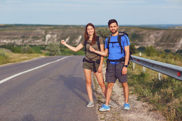 The guy and the girl are hitchhiking along the road.