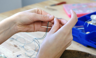 Close-up of a woman's hand stringing beads on the thread, making jewelry in the workshop.