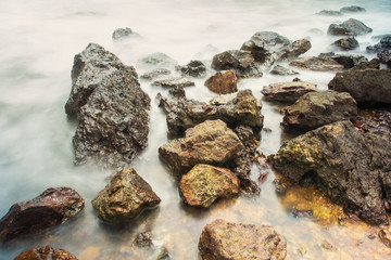 Long exposure seascape with foamy waves splashing against a rocky shore of thailand in the morning time.