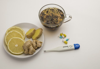 Folk remedies against colds, hot tea from herbs, lemon with ginger on a plate, medicines, thermometer on a white background.
