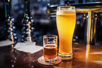 Light beer in a beer glass and dark beer in a small glass lighted with warm light on a bar counter