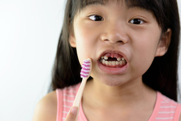 Little Asian girl without front teeth holding a tooth brush