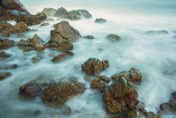 Long exposure seascape with foamy waves splashing against a rocky shore of thailand in the morning time.