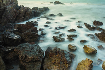 Long exposure seascape with foamy waves splashing against a rocky shore of thailand in the morning time.