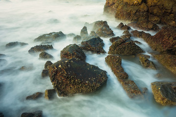 Long exposure seascape with foamy waves splashing against a rocky shore of thailand in the morning time.