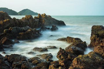 Long exposure seascape with foamy waves splashing against a rocky shore of thailand in the morning time.