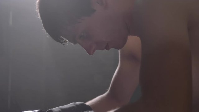 Profile of sweaty shirtless boxer sitting and getting up, going to fight, drop of water on his face