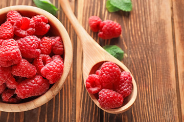 Bowl and spoon with sweet ripe raspberries on wooden background