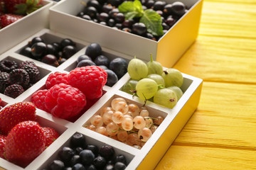 Boxes with delicious ripe berries on color table