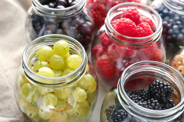 Fototapeta na wymiar Glass jars with delicious ripe berries on table, closeup