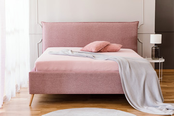 Real photo of pastel pink king-size bed with knit blanket and two pillows standing in bright...