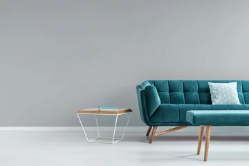 Fotobehang Metal and wood end table with book standing next to turquoise sofa with pillow in real photo of grey living room interior with place for your painting © Photographee.eu