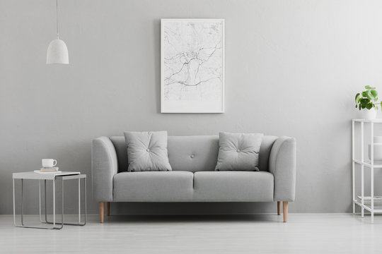 Poster above grey couch in minimal living room interior with lamp above table. Real photo