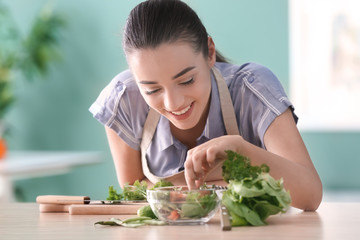Young woman preparing tasty salad with vegetables in kitchen