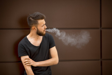 A young handsome white bearded man in black t-shirt smokes a cigarette in the street in the spring. Close up.