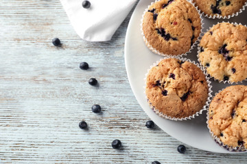 Plate with tasty blueberry muffins on wooden background