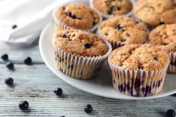 Plate with tasty blueberry muffins on wooden background