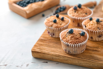 Wooden board with tasty blueberry muffins on table