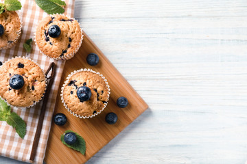 Wooden board with tasty blueberry muffins on table