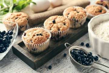 Wooden board with tasty blueberry muffins and fresh berries on table