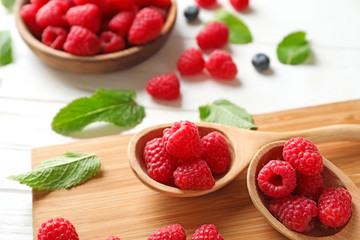 Spoons with fresh ripe raspberries on wooden board