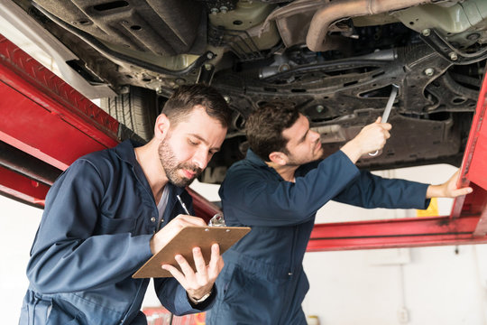 Mechanic Taking Notes While Coworker Repairing Car