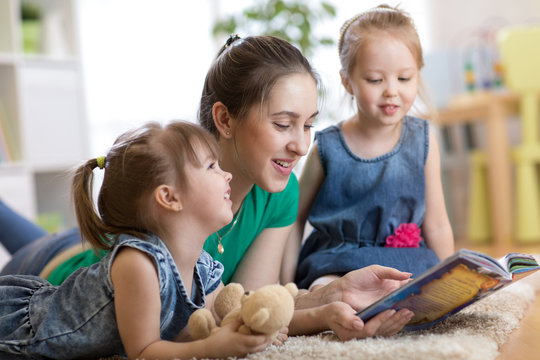 Young mom reads story to her little daughters. Family relaxing on floor