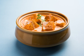 Paneer Butter Masala also known as Panir  makhani or makhanwala. served in a ceramic or terracotta bowl with fresh cream and coriander. Isolated over colourful moody background. selective focus