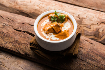 Paneer Butter Masala also known as Panir  makhani or makhanwala. served in a ceramic or terracotta bowl with fresh cream and coriander. Isolated over colourful moody background. selective focus