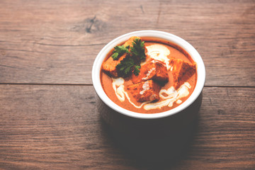 Paneer Butter Masala also known as Panir  makhani or makhanwala. served in a ceramic or terracotta bowl with fresh cream and coriander. Isolated over colourful moody background. selective focus
