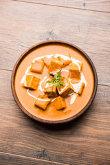 Paneer Butter Masala also known as Panir  makhani or makhanwala. served in a ceramic or terracotta bowl with fresh cream and coriander. Isolated over colourful moody background. selective focus