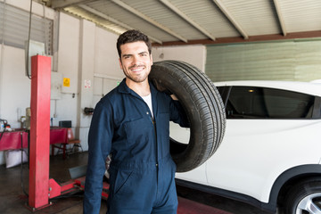 Fototapeta na wymiar Repairman Carrying Car Tire On Shoulder In Garage