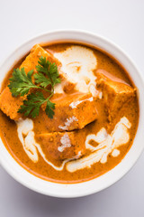 Paneer Butter Masala also known as Panir  makhani or makhanwala. served in a ceramic or terracotta bowl with fresh cream and coriander. Isolated over colourful moody background. selective focus