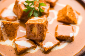 Paneer Butter Masala also known as Panir  makhani or makhanwala. served in a ceramic or terracotta bowl with fresh cream and coriander. Isolated over colourful moody background. selective focus