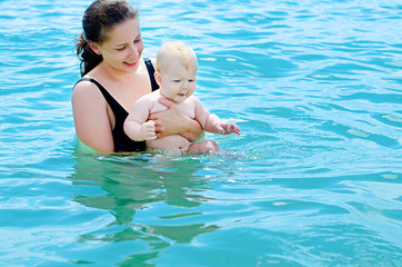 Happy mother  bathing her baby in azure sea water 