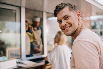 handsome young man smiling at camera while standing in line at food truck