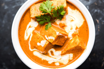 Paneer Butter Masala also known as Panir  makhani or makhanwala. served in a ceramic or terracotta bowl with fresh cream and coriander. Isolated over colourful moody background. selective focus
