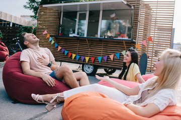 happy young friends laughing while sitting on bean bag chairs near food truck