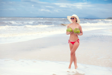 Happy young woman in straw hat with on the beach with a coconut drink