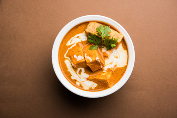 Paneer Butter Masala also known as Panir  makhani or makhanwala. served in a ceramic or terracotta bowl with fresh cream and coriander. Isolated over colourful moody background. selective focus