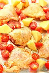 Seasoned chicken pieces with Yukon gold potatoes and cherry tomatoes on a sheet pan, vertical view
