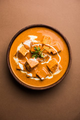 Paneer Butter Masala also known as Panir  makhani or makhanwala. served in a ceramic or terracotta bowl with fresh cream and coriander. Isolated over colourful moody background. selective focus