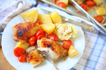Plate of roast chicken with cabbage, potatoes and cherry tomatoes on a dish towel