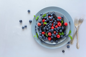 Fruit salad with blackberry, blueberry, raspberry and mint leaves on wooden gray background. Flat lay. Top view